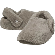 Load image into Gallery viewer, A pair of plush, fuzzy slip-on slippers in a light taupe-beige color, featuring a small clear rhinestone button on the strap of one slipper, set against a solid black background.
